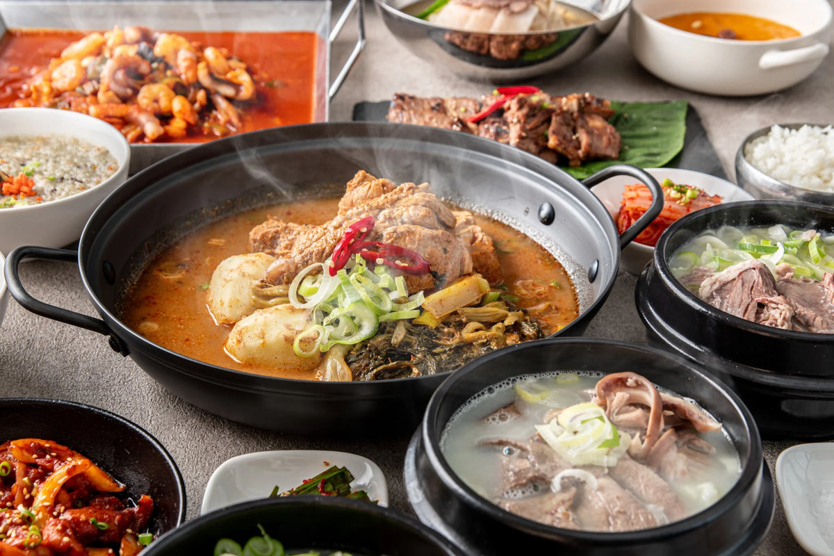 湯気の立つ鍋とクッパを囲む、bibim'の韓国料理の食卓